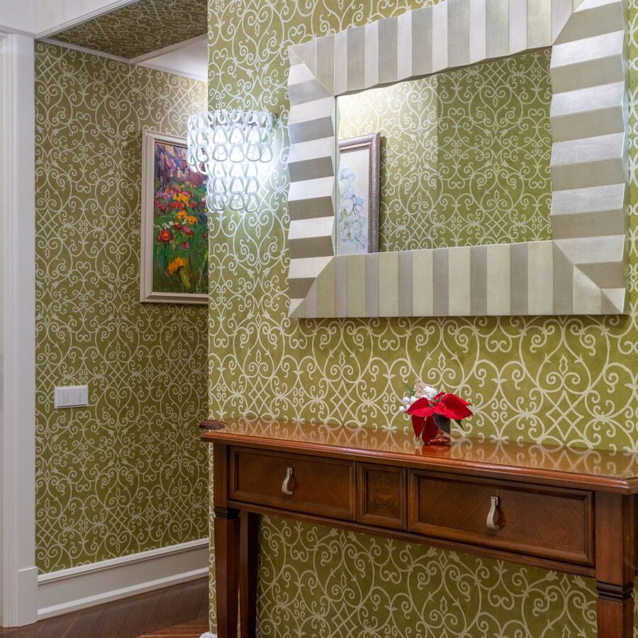 Green patterned wallpaper behind a wooden console table and mirror